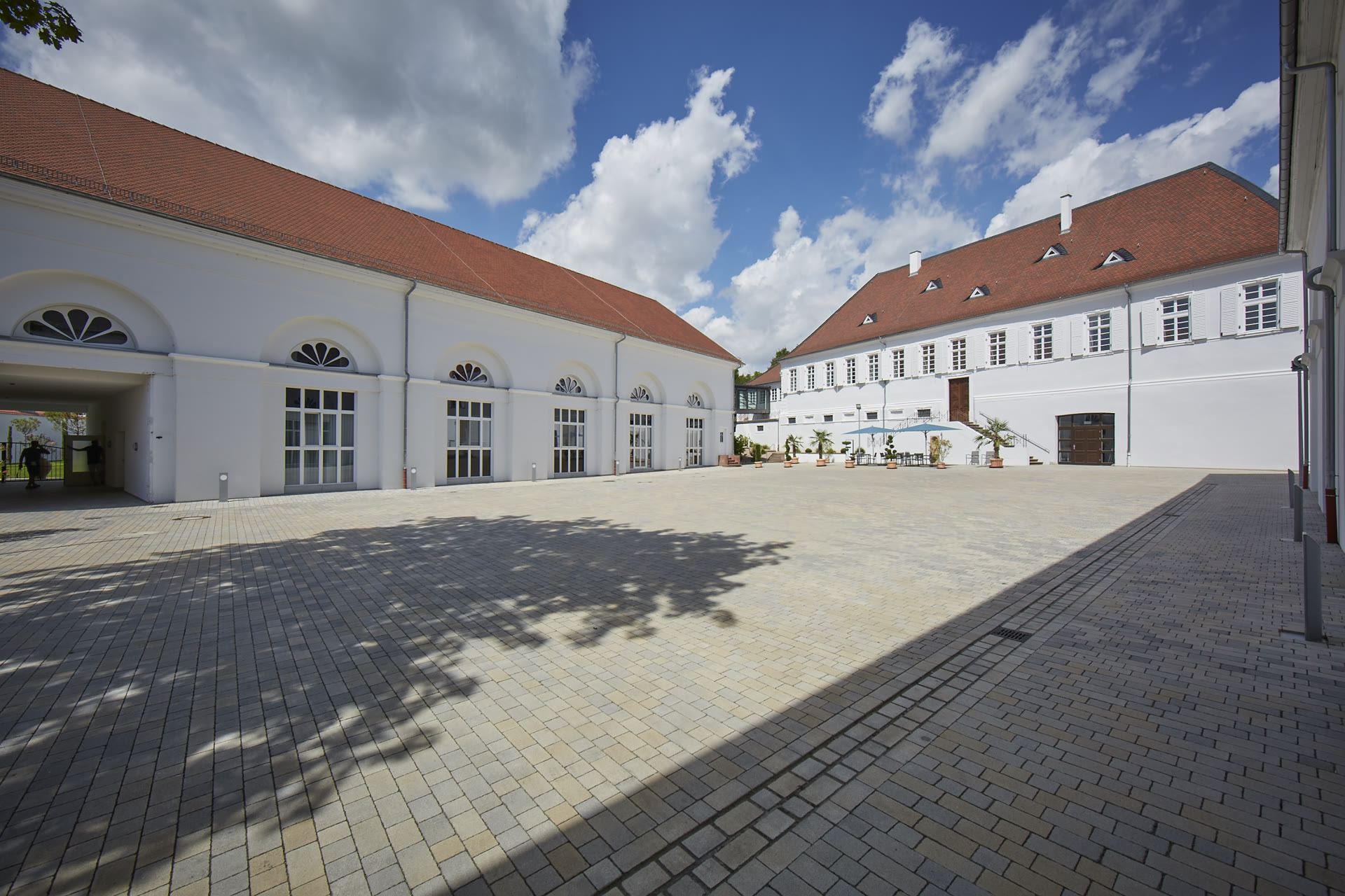 Sanierte Westremise mit weißer Fassade, Rundbogenfenstern und großen Glastüren