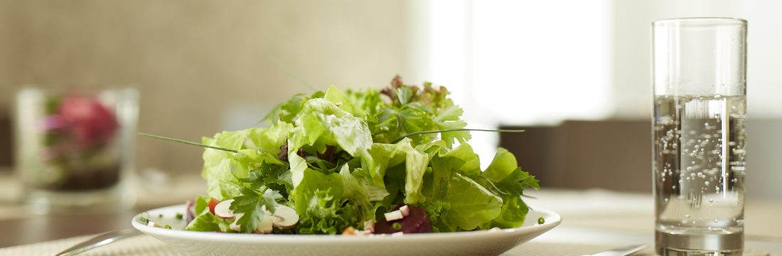 Angerichteter Salatteller mit Wasserglas auf einem Tisch im Restaurant
