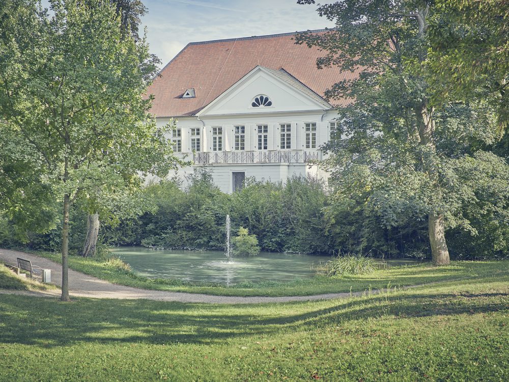Blick über den Weiher im Schlosspark auf das historische Herrenhaus